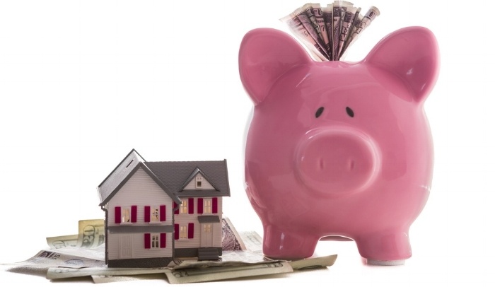 Close up of a pink piggy bank with dollars beside miniature house model on white background-858378-edited.jpeg